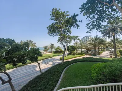 a walkway through a park with palm trees and the ocean at Bright 2 Bedroom Apartment, Beach & Pool Access in Dubai