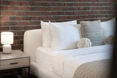 a white bed with white pillows and a brick wall at 1-Bedroom Apartment with Greenery & City Views in The Terraces in Dubai
