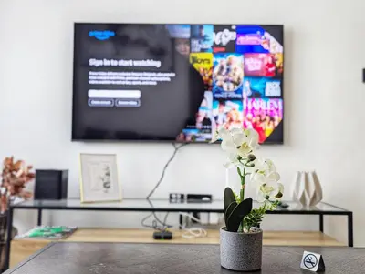 a table with a vase with white flowers in front of a tv at Modern Luxury Fully Furnished 1BH Apartment in Binghatt Nova JVC - Easy Access to JBR, Circle Mall & Dubai Hills Mall in Dubai
