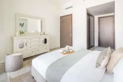 a white bedroom with a large bed and a dresser at Frank Porter - Boulevard Heights in Dubai