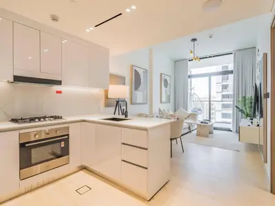 a kitchen with white cabinets and a living room at TRPS - Binghatti Emerald, Jumeirah Village Circle - Luxury 1BR Haven in Dubai