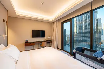 a hotel room with a bed and a desk and a window at Venetian - Stay at Address Opera with Burj & Fountain views in Dubai