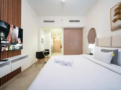 a white bedroom with a large bed and a desk at Sleek Studio in Azizi Riviera Modern and Cozy Stay in Dubai