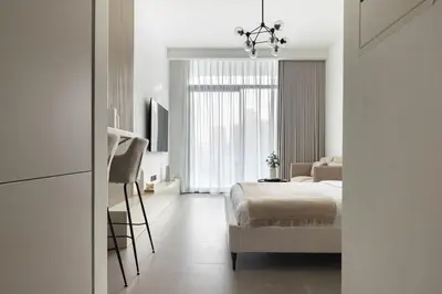 a white bedroom with a bed and a chair at Modern Studio Apartment JVC in Dubai