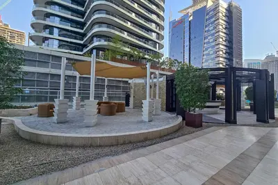 a building with a pavilion in a city with tall buildings at EasyGo - Chic 1BR in Damac Maison in Dubai