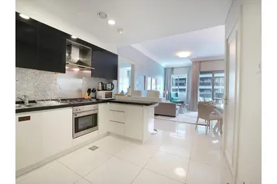 a kitchen with white appliances and a living room at EasyGo - Chic 1BR in Damac Maison in Dubai