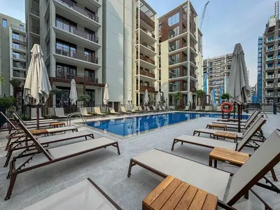 a pool with chairs and umbrellas in a building at Elegant 1BR with Pool, Gym Access and Kid's Play Area in Dubai