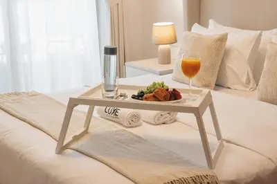 a tray of food and a glass of wine on a bed at JBR Rimal By Luxe Living - Dubai Eye View in Dubai