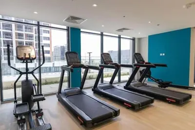 a gym with three treadmills in a room with windows at Modern Studio in Azizi Riviera, Meydan in Dubai