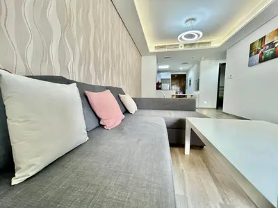 a living room with a gray couch with a pink pillow at Homes2Retreat - Serene 1BR Getaway with Stunning Views in Dubai