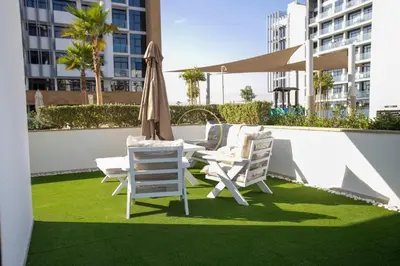 a patio with chairs and an umbrella and grass at 3BHK Apartment located in Azizi riviera 34 in Dubai