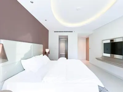 a white bedroom with a large bed and a flat screen tv at 2BR Apartment in Paramount Tower in Dubai
