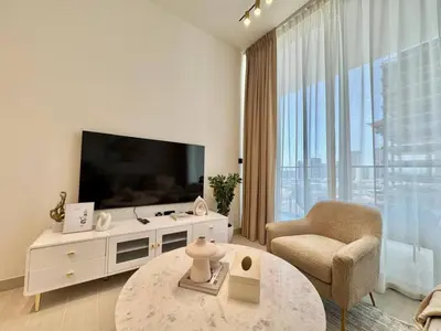 a living room with a television and a chair and a table at Chic Jvc 1br Pool Access, Balcony & Parking in Dubai