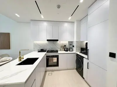 a white kitchen with white cabinets and a sink at Chic Jvc 1br Pool Access, Balcony & Parking in Dubai