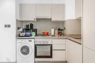 a white kitchen with a stove and a washer at Stylish 1BR with Pool, BBQ Area, Gym in MBR City in Dubai