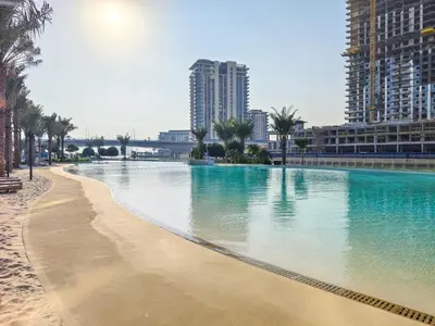 a large swimming pool next to a beach with tall buildings at Beach Escape 1BR-Vida Residences Creek Beach in Dubai
