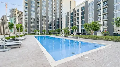 a swimming pool with chairs and umbrellas and buildings at Escape24 Elegant 2BR with Garden View in Dubai Hills in Dubai