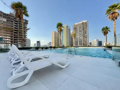 a pool with white lounge chairs and palm trees and buildings at Brand New-Fully Furnished Classy Studio In JVC in Dubai