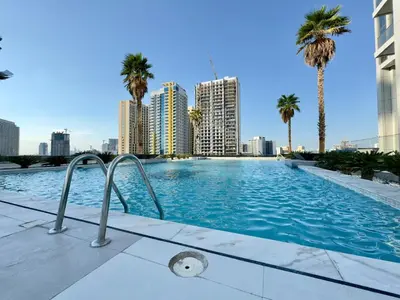 a swimming pool with palm trees and buildings at Brand New-Fully Furnished Classy Studio In JVC in Dubai