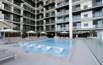 a large swimming pool with white chairs and a building at Elegant Jvc 1br Balcony, Pool Access, Parking in Dubai