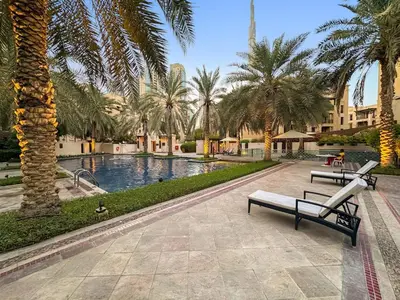 a resort with a pool with palm trees and benches at Charming Old Town Dubai 2BR Retreat with Burj Khalifa Balcony View in Dubai