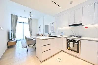 a kitchen with white cabinets and a living room at Stunning 1 Bdr luxury residence at JVC in Dubai