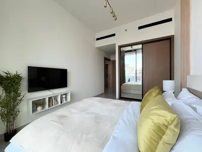a white bedroom with a large bed with a tv on the wall at Peaceful 1br Jvc Pool, Balcony, Parking in Dubai