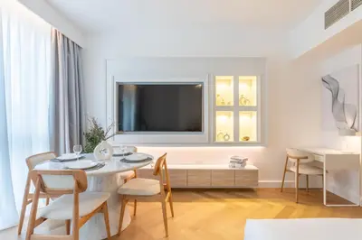 a white living room with a table and a tv at Vacationer I Luxe Studio I Steps to Burj Khalifa & Dubai Mall I Free Parking, Pool, Gym & Wi-Fi in Dubai