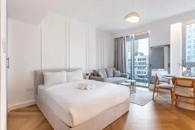 a white bedroom with a bed and a living room at Vacationer I Luxe Studio I Steps to Burj Khalifa & Dubai Mall I Free Parking, Pool, Gym & Wi-Fi in Dubai
