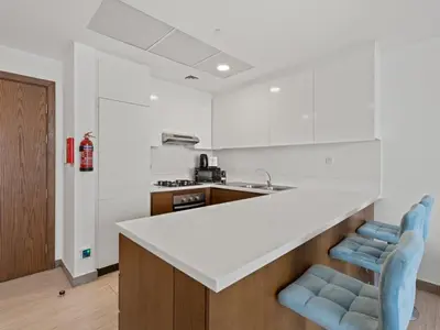 a kitchen with a white counter and two blue chairs at Spacious and Cozy 1BDR in Hameni in Dubai