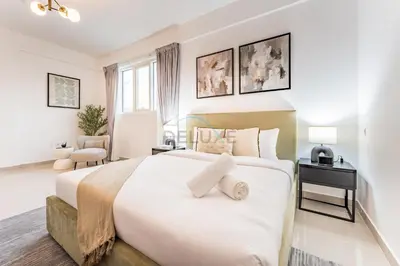 a white bedroom with a large bed and a chair at City View 2BR Just Steps from the Mall, Roxana Residence B, Jumeirah Village Circle by Deluxe Holiday Homes in Dubai