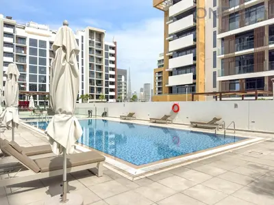 a swimming pool with chairs and umbrellas on a building at Cozy Studio Apartment in Meydan in Dubai