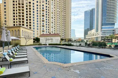 a swimming pool with chairs and buildings in a city at Cozy Beachside 1-bedroom in Murjan in Dubai