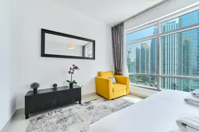 a bedroom with a yellow chair and a large window at 2BR at Lofts West Near Dubai Mall and Burj Khalifa in Dubai