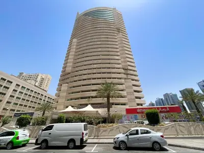a tall building with cars parked in a parking lot at 1 Bedroom in Dubai Marina opp Dmcc metro station in Dubai