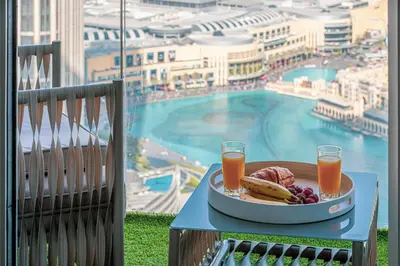 a table with a plate of food and drinks and a pool at Stunning Downtown 4BR Sky High Luxury Apartment with Fountain Views in Dubai