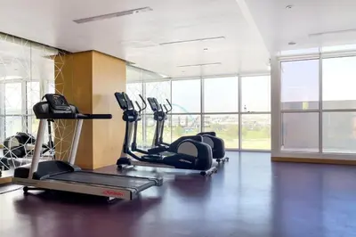 a gym with several tread machines in a room with windows at High-Rise Studio Near the Golf Club and Mall with a Community View,Damac Hills Artesia Tower D, Dubailand by Deluxe Holiday Homes in Dubai