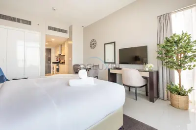a white bedroom with a large bed and a desk at High-Rise Studio Near the Golf Club and Mall with a Community View,Damac Hills Artesia Tower D, Dubailand by Deluxe Holiday Homes in Dubai