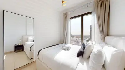 a white bedroom with a large window with white pillows at UNA Tower - Peaceful One Bedroom in Townsquare in Dubai