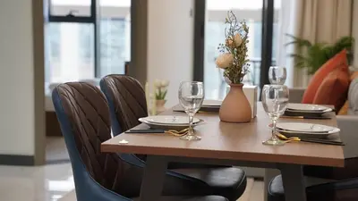 a wooden table with wine glasses and a vase with flowers at Daraqa - Modern 1BR Apartment in Peaceful Dubai Land in Dubai