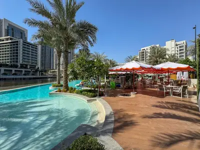 a swimming pool with tables and umbrellas and buildings at Vibrant 1BR With Airy Patio, Beach, Pool and Gym Access in Dubai