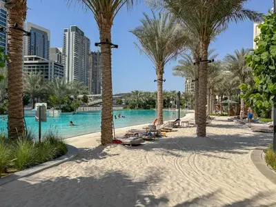 a pool with palm trees and people in the water at Vibrant 1BR With Airy Patio, Beach, Pool and Gym Access in Dubai