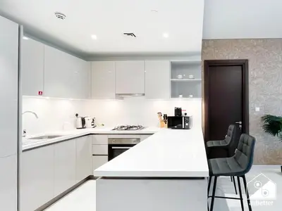 a white kitchen with white cabinets and a black chair at Spacious 2B in Sobha Creek Vistas ,Dubai in Dubai