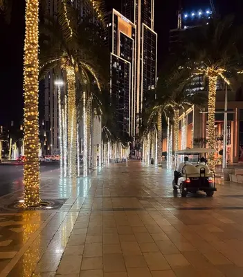 an empty street at night with palm trees and lights at 29 Boulevard by EMAAR 1BR 4min Walk to the Burj and Dubai Mall in Dubai