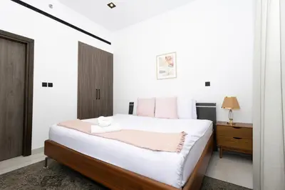 a white bedroom with a bed and a nightstand at Spacious 2BR Apartment l Rooftop Pool l Gym in Dubai