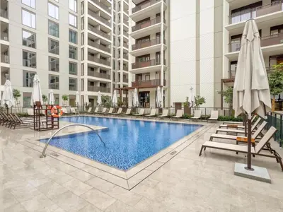 a swimming pool with chairs and umbrellas next to a building at FAM Living - Modern 1BR at Orchid, Creek Harbour in Dubai