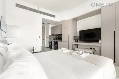 a white bedroom with a large bed and a television at Modern Cozy Studio in Dubai