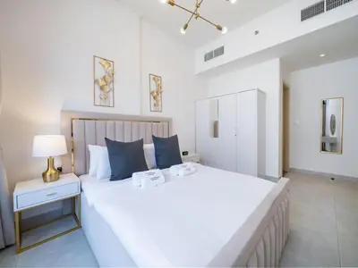 a white bedroom with a large white bed and a lamp at Bright and Spacious 1 Bed Prime JVC Location in Dubai