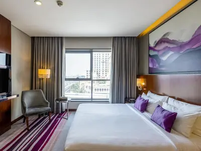 a hotel room with a large bed with purple pillows at Flora Al Barsha Hotel At The Mall in Dubai