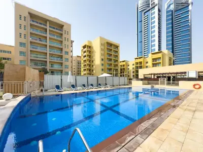 a large swimming pool with chairs and buildings at Vogue The Greens Al Alka near Mall of the Emirates, One Bedroom Apartment with Balcony and Vibrant community View, Access to all Amenities in Dubai